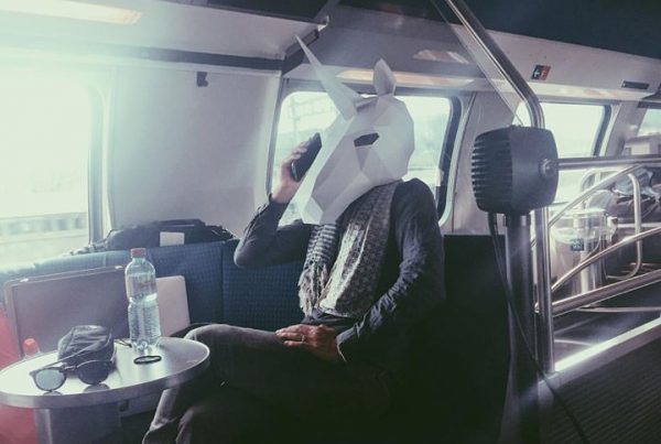person with a paper unicorn head sitting and using the selfphone